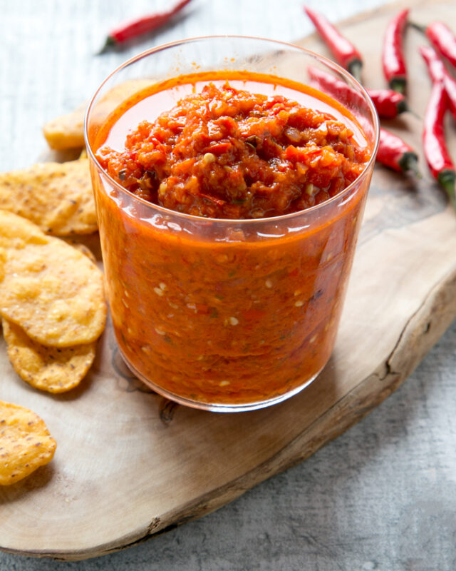 per peri sauce in a tall glass, tortilla chips and chili peppers in the background