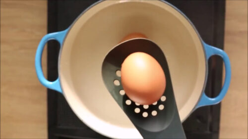 egg in a slotted spoon lowered into the pot of water