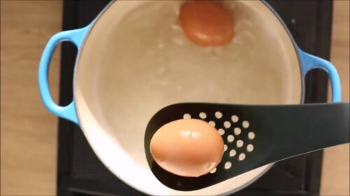 egg in a slotted spoon removed from the pot of water