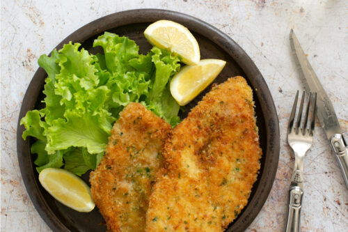 breaded chicken cutlets on a plate with lemon wedges and salad