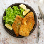 italian breaded chicken cutlets on a plate with lemon wedges and salad