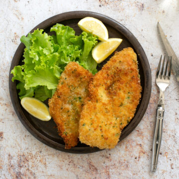 italian breaded chicken cutlets on a plate with lemon wedges and salad