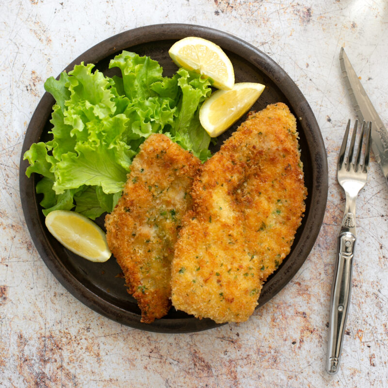 italian breaded chicken cutlets on a plate with lemon wedges and salad