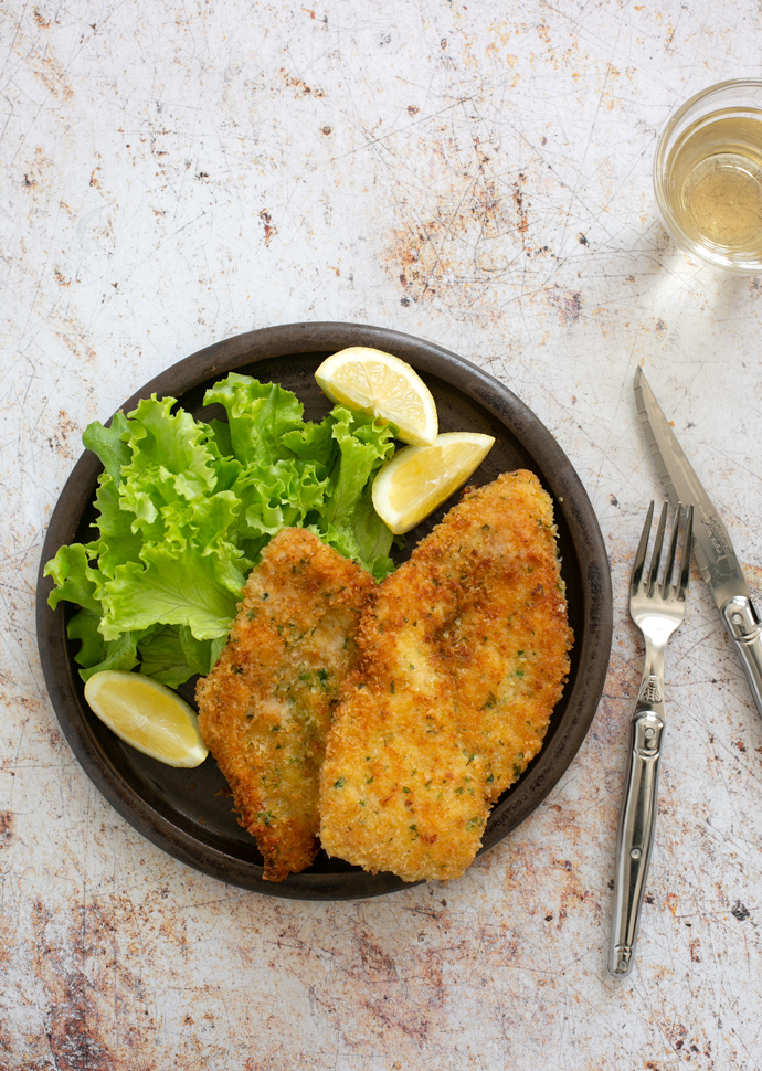 Italian chicken cutlets served with green salad and lemon wedges.