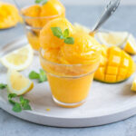 vegan mango sorbet divided among two glasses, topped with mint leaves