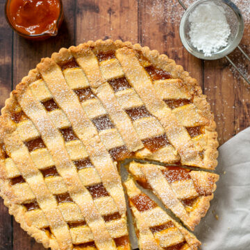 italian jam tart with 2 slices cut ready to be served. Confectioner sugar and peach jam on the side.