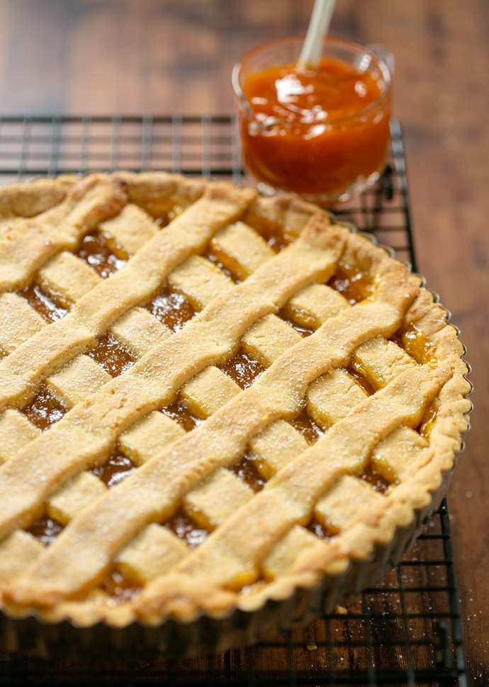 crostata out of the oven resting on a cooling rack, peach jam on the side.