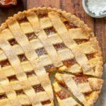 italian jam tart with 2 slices cut ready to be served. Confectioner sugar and peach jam on the side. Image for Pinterest.