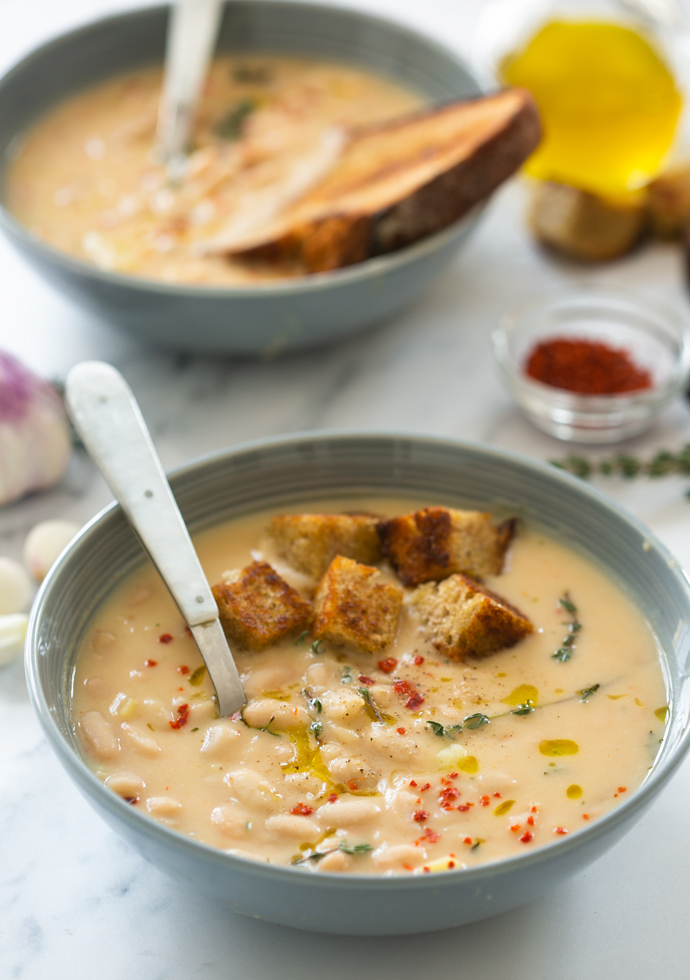 bowl of creamy cannellini soup topped with croutons, olive oil, thyme leaves and red chili flakes.