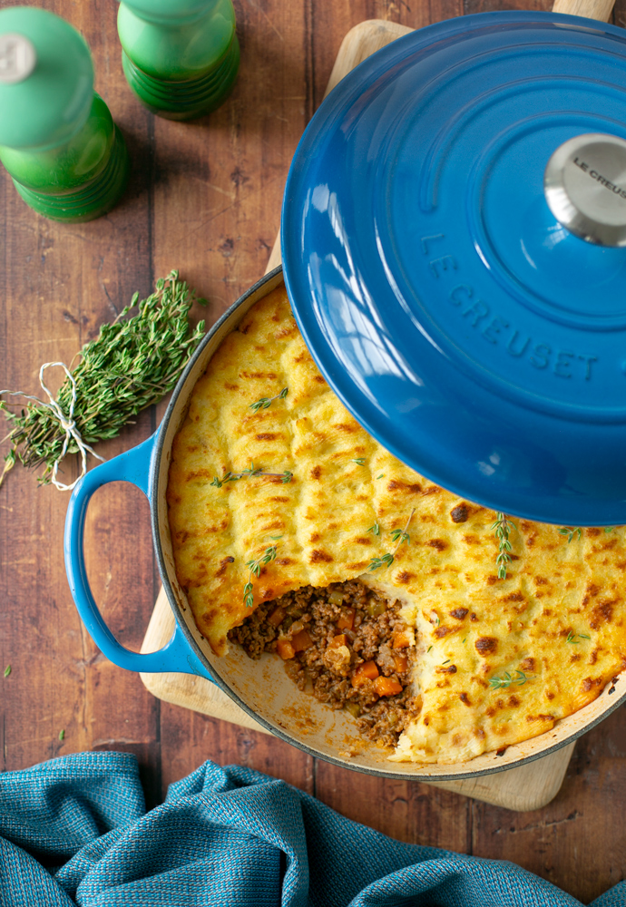 cottage pie in a cast iron casserole pot, topped with fresh thyme sprigs.