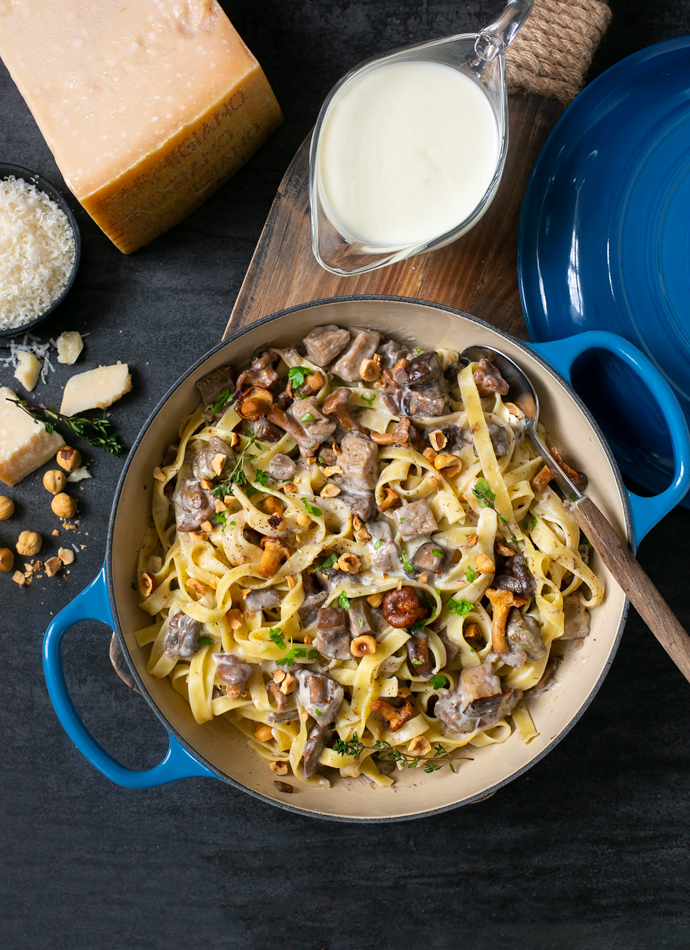tagliatelle pasta with parmesan sauce, wild mushrooms and roasted hazelnuts, in a large cast iron shallow pot. Served next Parmigiano Reggiano cheese wedge and extra sauce on the side.