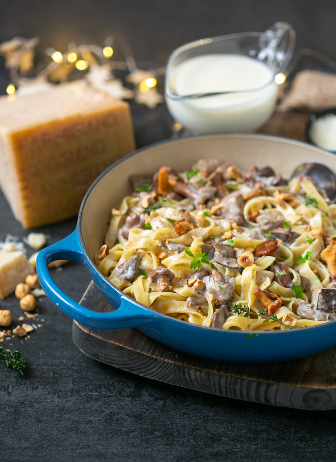 tagliatelle pasta with parmesan sauce, wild mushrooms and roasted hazelnuts, in a large cast iron shallow pot. Served next Parmigiano Reggiano cheese wedge and extra sauce on the side.