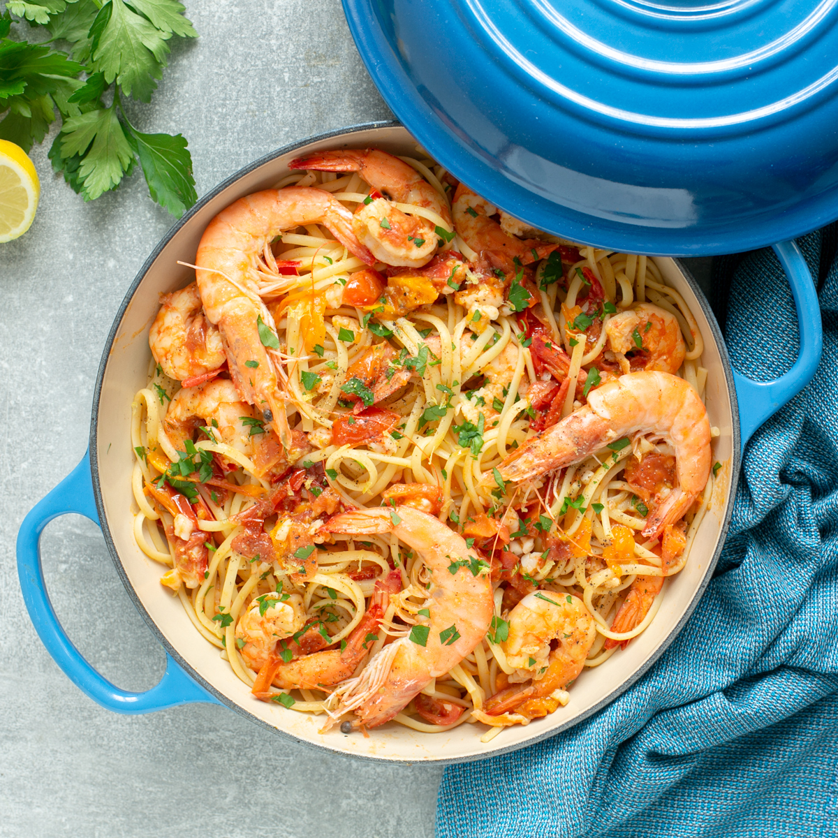 Shrimp linguine in a shallow casserole pot, topped with chopped parsley and whole king prawns.
