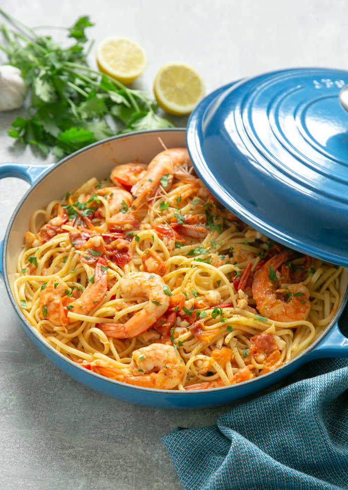 shrimp pasta in a shallow casserole pot, topped with chopped parsley and whole king prawns.