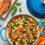 sweet potato penne pasta with crispy prosciutto adn sauteed spinach leaves served in a large pot. Image optimized for Pinterest.