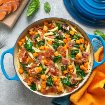 sweet potato penne pasta with crispy prosciutto adn sauteed spinach leaves served in a large pot.
