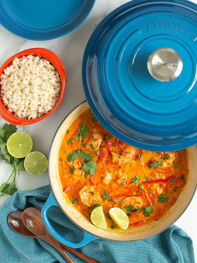 Prawn curry topped with lime wedges and fresh coriander served in a large skillet, with brown rice on the side.