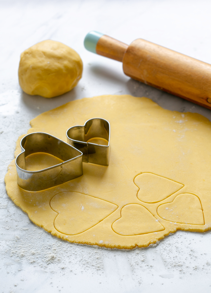 italian pastry dough rolled into a disk being cut with heart-shaped cookie cutters.