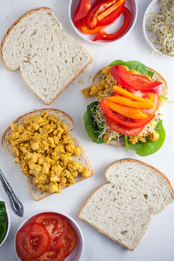 Curried chickpea salad on sandwich slices, topped with lettuce and peppers.