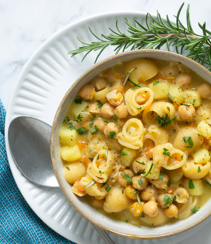 pasta and chickpea soup topped with chopped rosemary in a bowl.