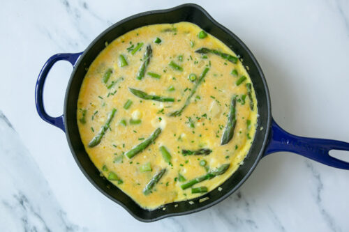 egg mixture covering the aspragus in the skillet.