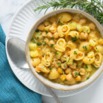pasta and chickpea soup topped with chopped rosemary in a bowl.