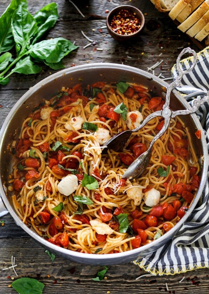 vegan caprese pasta in a pan, topped with vegan mozzarella and basil leaves.