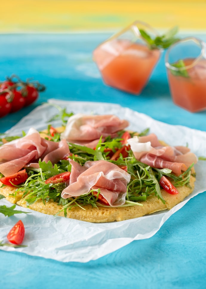 Socca pizza topped with rocket leaves, cherry tomatoes and Parma Ham slices.