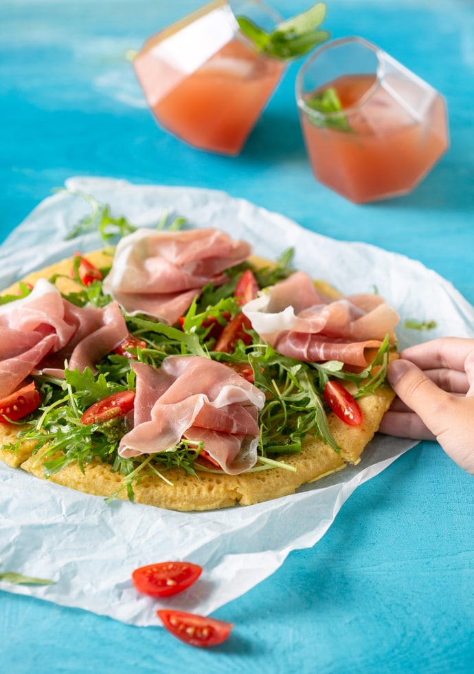 Chickpea flatbread pizza topped with Parma Ham, rocket leaves and cherry tomatoes.