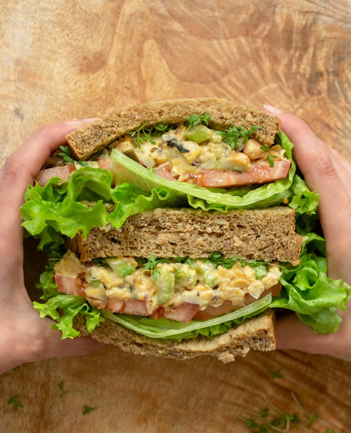 hands holding a vegan chickpea salad sandwich.