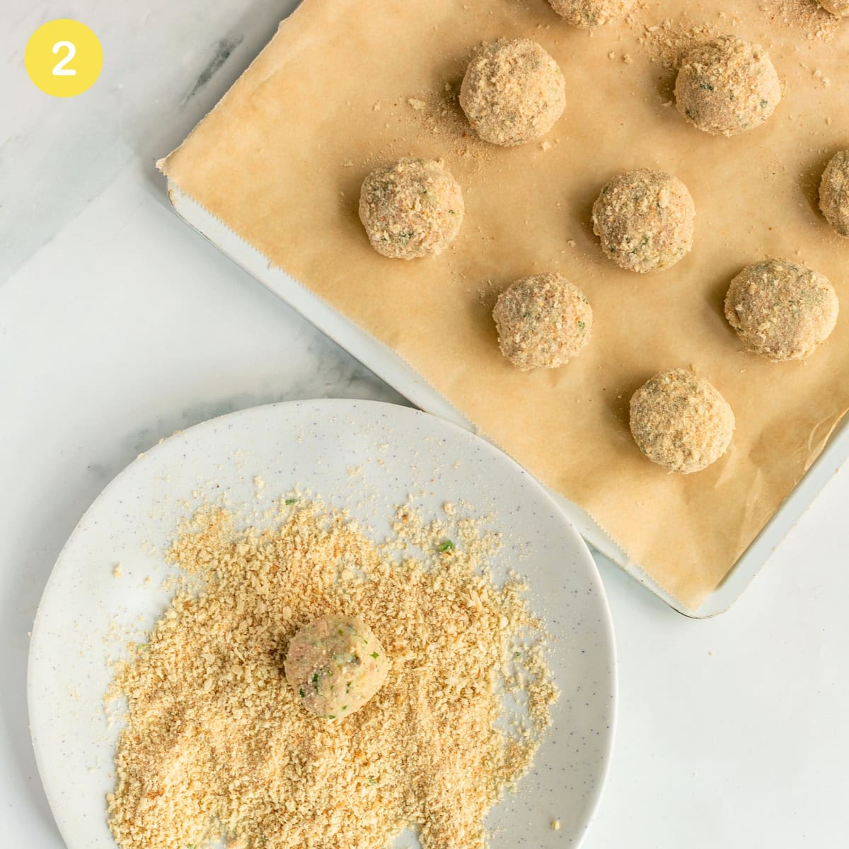 Formed tuna fish meatballs rolled in breadcrumbs, placed on a parchment-lined baking tray.