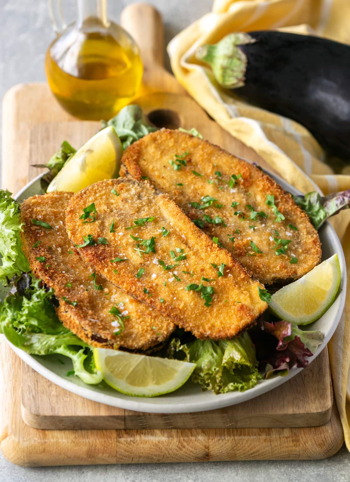 Crispy eggplant cutlets served on a bed of fresh salad with lemon wedges and olive oil.
