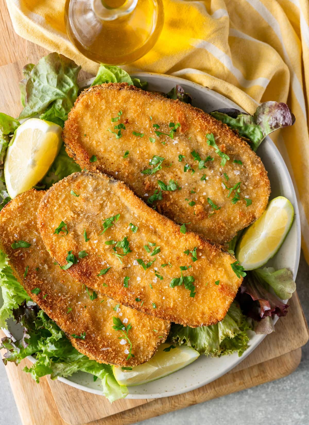 Italian eggplant Milanese on a plate with lettuce, lemon wedges, and olive oil bottle.