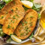 Italian eggplant cutlets served on a bed of fresh salad with lemon wedges and olive oil.