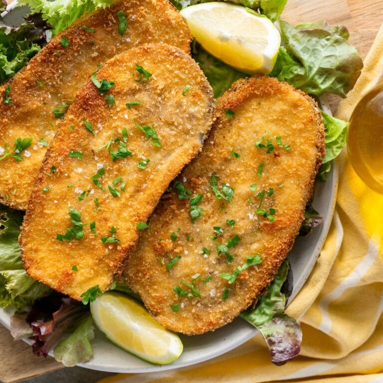 Italian eggplant cutlets served on a bed of fresh salad with lemon wedges and olive oil.