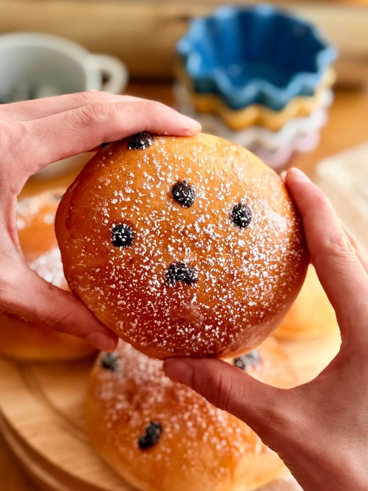 Hands holding a golden pangocciolo dusted with powdered sugar, with chocolate chips on top