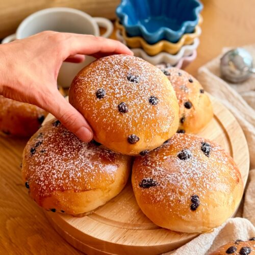 Golden chocolate milk buns dusted with powdered sugar, rom a pile of homemade pangoccioli on a wooden board.